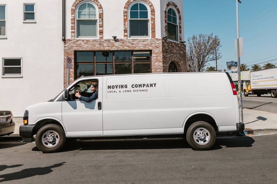 A person wearing a black face mask, grey cap, yellow padded vest over a grey long-sleeve shirt, and black gloves is seen stepping out of a white cargo van, holding a brown paper bag in their left hand