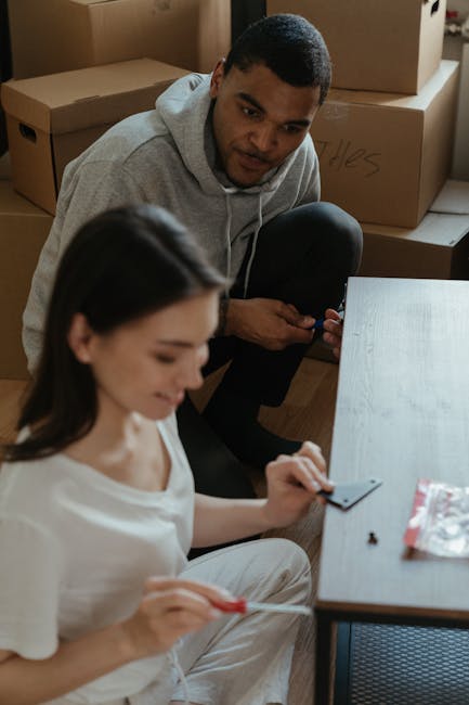 A white moving van parked on an elevated area during dusk or early evening, with its side door open revealing a wooden chair among packed cardboard boxes and protective wrapping materials inside. The 